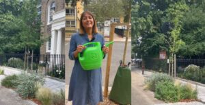 Cllr Rezina Chowdhury holds watering can next to street tree