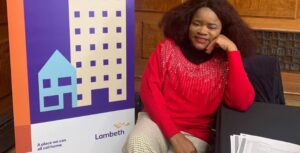 Lady of West African heritage wearing red sparkley jumper smiles at camera.