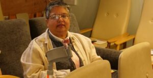 Lady in her sixties sitting in chair holding a crutch.