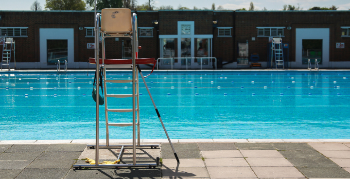 A Lido - outside swimming pool with lifeguard chair in foreground - in the distance the pool glistening in the sunshine, the lane markers are clear and the depths of water are just visible.