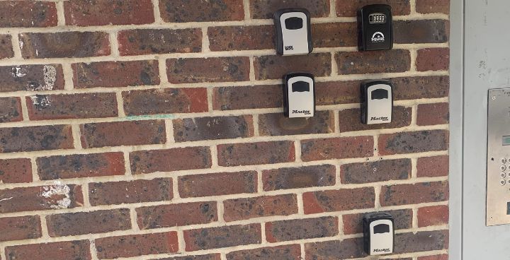 5 lock boxes for keys attached to the wall next to the communal entrance of an estate